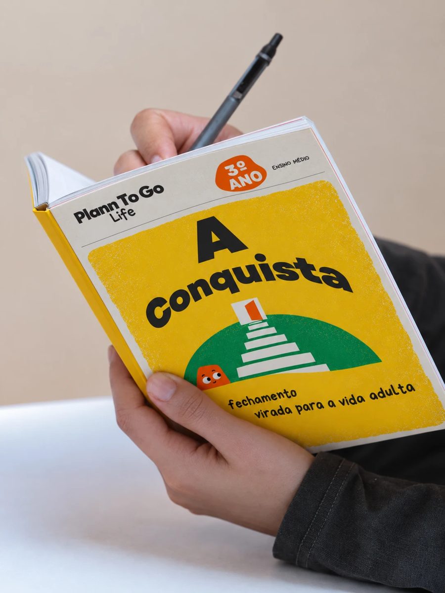 Estudante segurando o livro A Conquista, do 3º ano do Ensino Médio da Plann To Go Life, com uma caneta na mão.